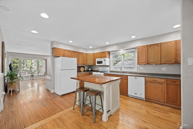 kitchen featuring white appliances, a sink, light wood finished floors, a kitchen bar, and recessed lighting