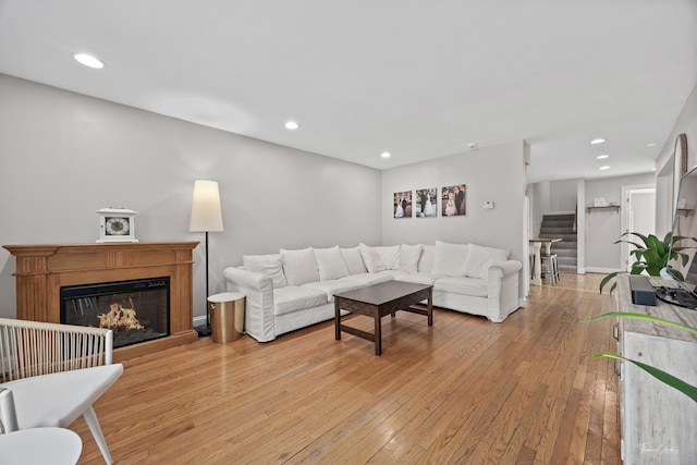 living area with light wood-style flooring, stairway, a glass covered fireplace, recessed lighting, and baseboards