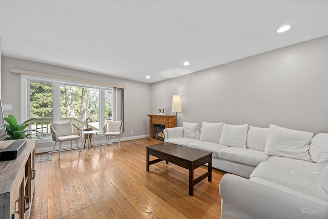 living room with light wood-style floors, a glass covered fireplace, baseboards, and recessed lighting