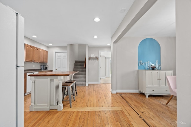 kitchen featuring light wood-style flooring, a kitchen breakfast bar, baseboards, recessed lighting, and freestanding refrigerator