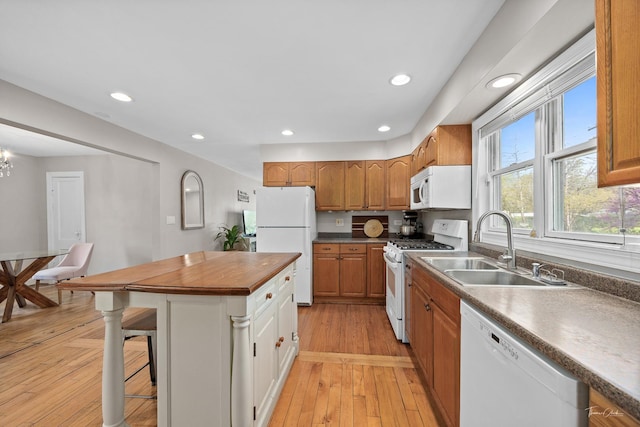 kitchen with white appliances, a sink, a kitchen island, a kitchen bar, and light wood-style flooring
