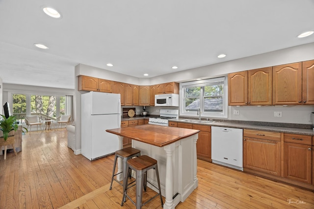 kitchen with white appliances, light wood finished floors, recessed lighting, a breakfast bar area, and a sink