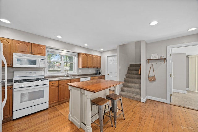 kitchen featuring white appliances, a sink, a kitchen bar, light wood-style floors, and baseboards