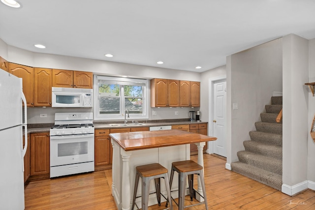kitchen with white appliances, a sink, light wood finished floors, a kitchen bar, and recessed lighting