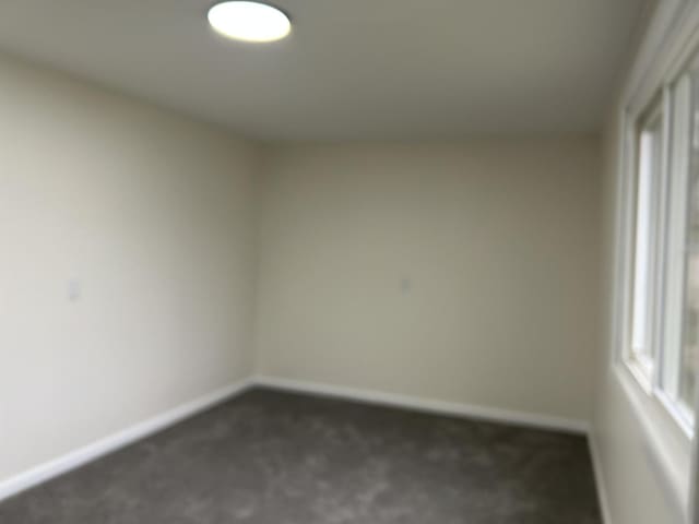 unfurnished room featuring dark colored carpet and baseboards