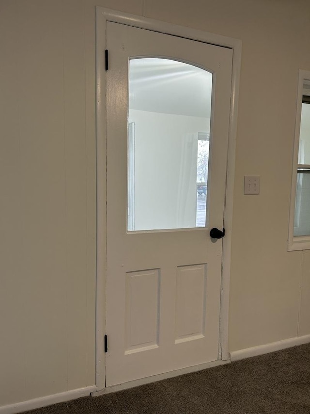 doorway featuring baseboards and dark carpet