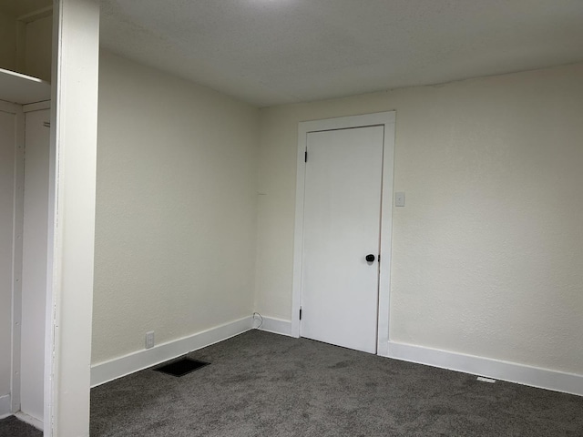 empty room featuring dark carpet, baseboards, and visible vents