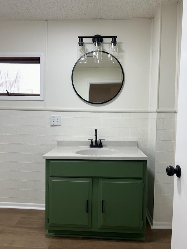 bathroom featuring wood finished floors, tile walls, vanity, and a drop ceiling