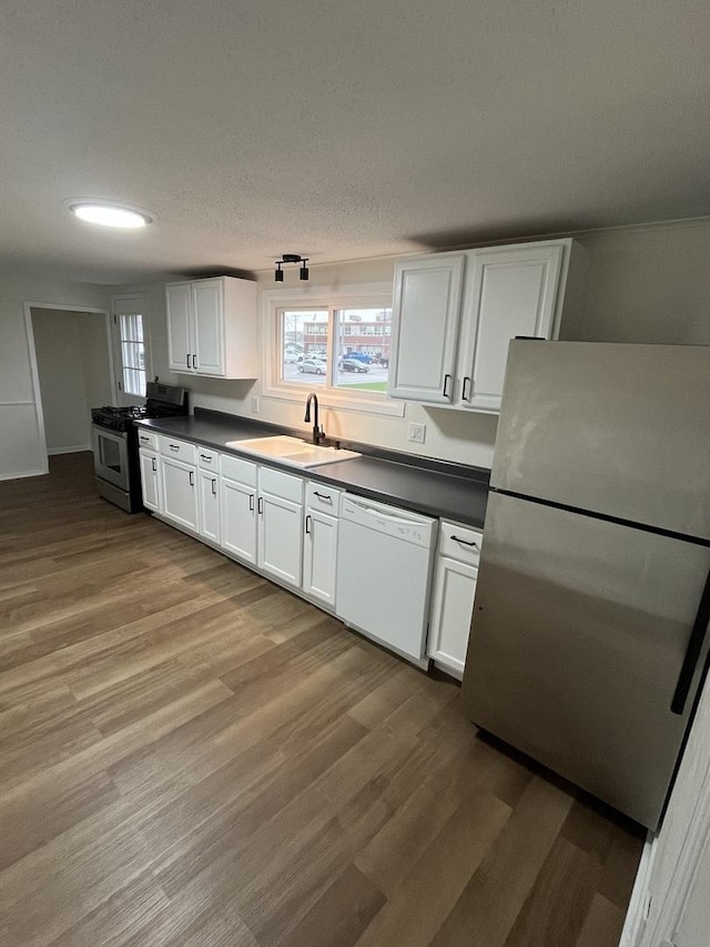 kitchen featuring dark countertops, wood finished floors, stainless steel appliances, and a sink