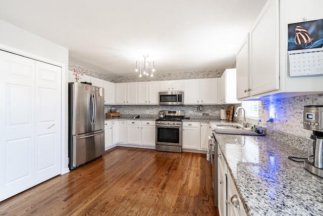 kitchen with dark wood-style floors, light stone counters, stainless steel appliances, a sink, and a chandelier