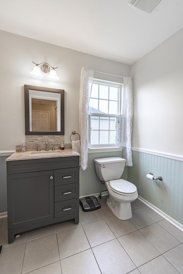 half bath featuring tile patterned flooring, a wainscoted wall, visible vents, toilet, and vanity