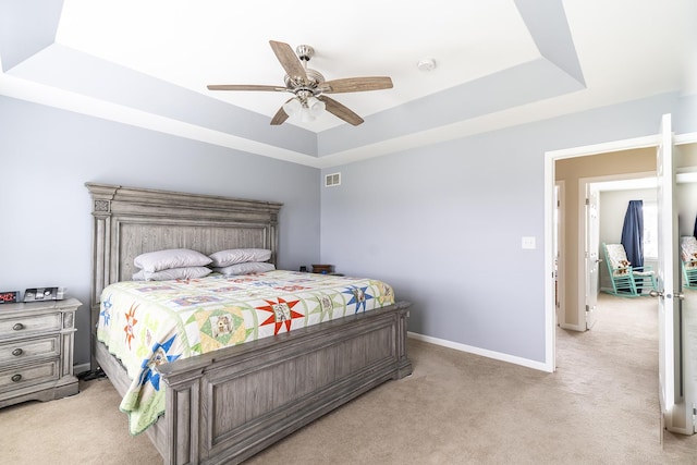 bedroom with ceiling fan, a tray ceiling, light colored carpet, baseboards, and visible vents