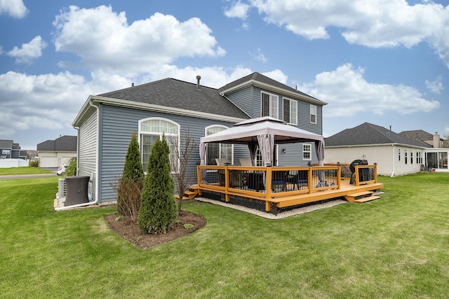 rear view of house with a lawn, a gazebo, a deck, and a shingled roof