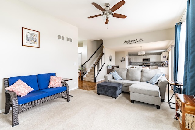 living room featuring baseboards, visible vents, light colored carpet, a ceiling fan, and stairway