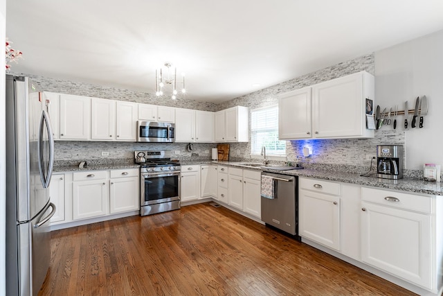 kitchen featuring white cabinets, stainless steel appliances, tasteful backsplash, a chandelier, and light stone counters
