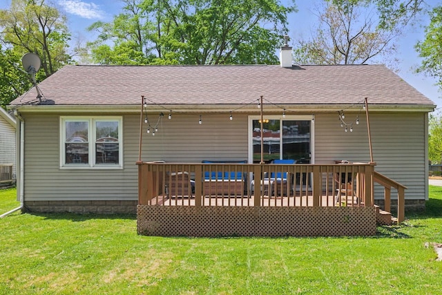 rear view of house with a chimney, a deck, a yard, and roof with shingles