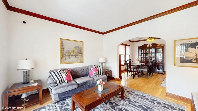 living room featuring arched walkways, baseboards, ornamental molding, and wood finished floors