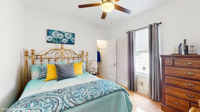 bedroom with a ceiling fan, wood finished floors, baseboards, a closet, and a spacious closet