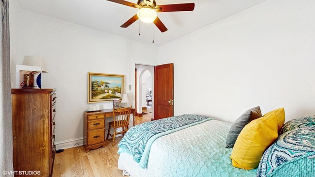 bedroom with crown molding, a ceiling fan, baseboards, arched walkways, and light wood-style flooring