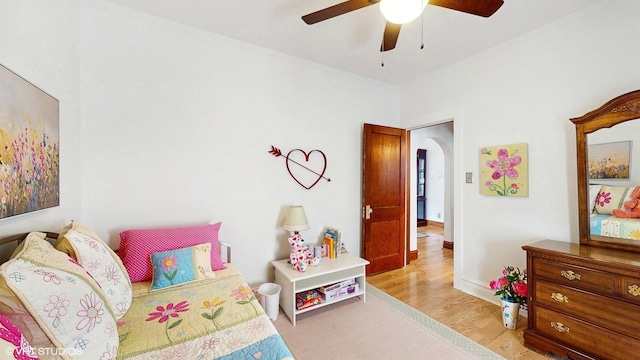 bedroom with baseboards, arched walkways, light wood finished floors, and a ceiling fan