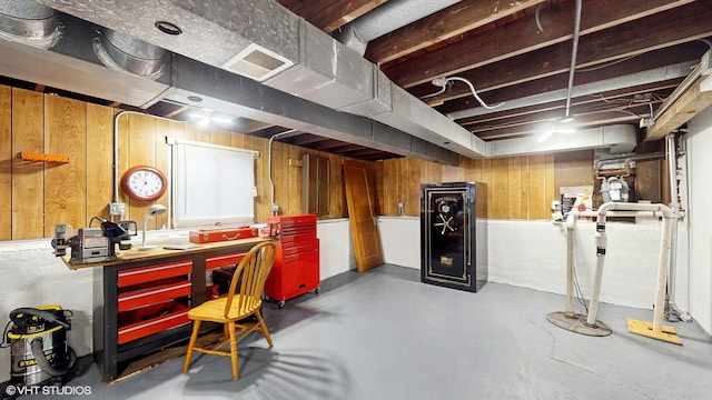 unfinished below grade area featuring wooden walls, a workshop area, and visible vents