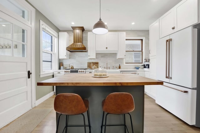 kitchen featuring white cabinets, white appliances, butcher block counters, a breakfast bar, and premium range hood