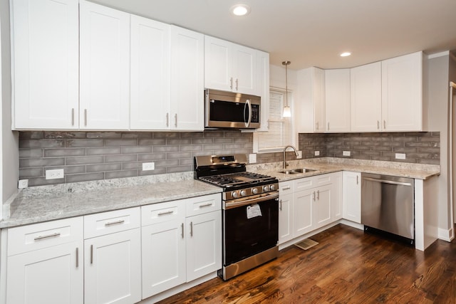 kitchen with a sink, dark wood finished floors, white cabinetry, light stone counters, and appliances with stainless steel finishes