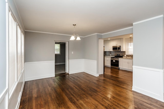 unfurnished dining area featuring wainscoting, ornamental molding, a chandelier, and dark wood-style floors