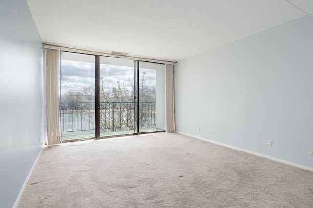 carpeted spare room featuring a wall of windows, visible vents, and baseboards