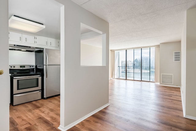 kitchen with white cabinets, range hood, visible vents, expansive windows, and appliances with stainless steel finishes