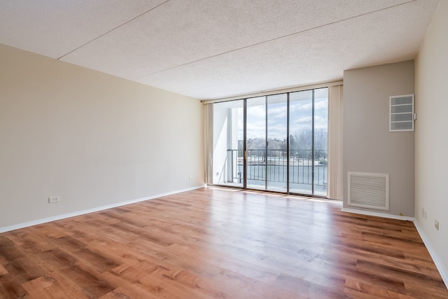 empty room with wood finished floors, a textured ceiling, visible vents, and a wall of windows