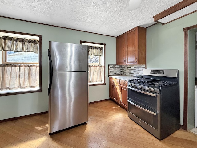 kitchen with brown cabinets, baseboards, appliances with stainless steel finishes, and light wood-type flooring