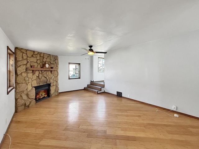 unfurnished living room featuring visible vents, baseboards, wood finished floors, ceiling fan, and a fireplace