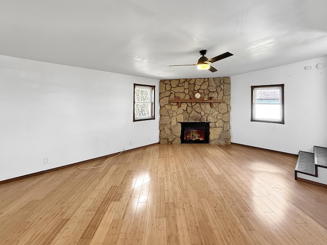 unfurnished living room featuring a fireplace, a ceiling fan, light wood finished floors, and plenty of natural light