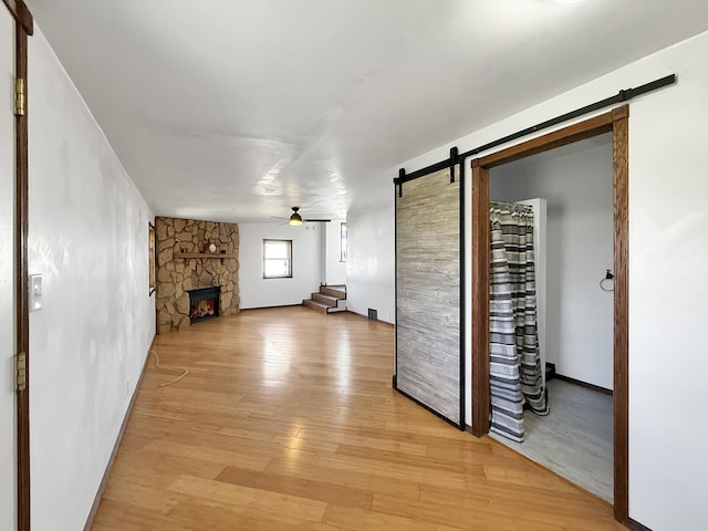 unfurnished living room featuring light wood-type flooring, a ceiling fan, a fireplace, and a barn door