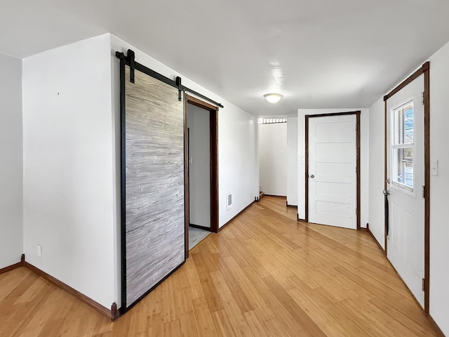 spare room featuring light wood-type flooring, baseboards, visible vents, and a barn door