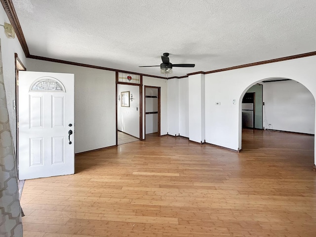 interior space with a ceiling fan, a textured ceiling, light wood-style floors, arched walkways, and ornamental molding