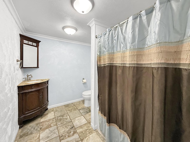 bathroom with toilet, vanity, stone tile flooring, crown molding, and baseboards