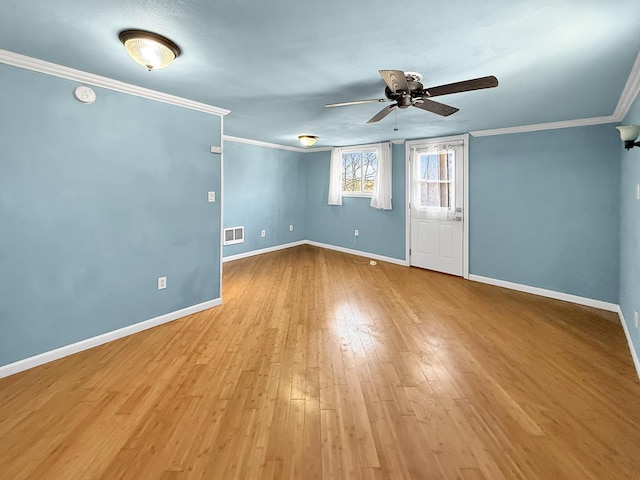 empty room with baseboards, visible vents, a ceiling fan, wood finished floors, and crown molding