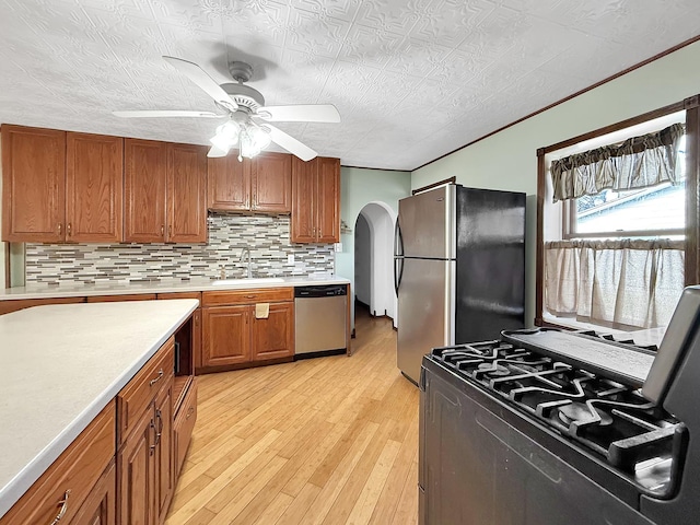 kitchen with light countertops, a ceiling fan, a sink, arched walkways, and appliances with stainless steel finishes