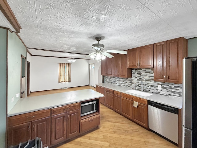 kitchen with a ceiling fan, a sink, decorative backsplash, light wood-style flooring, and appliances with stainless steel finishes
