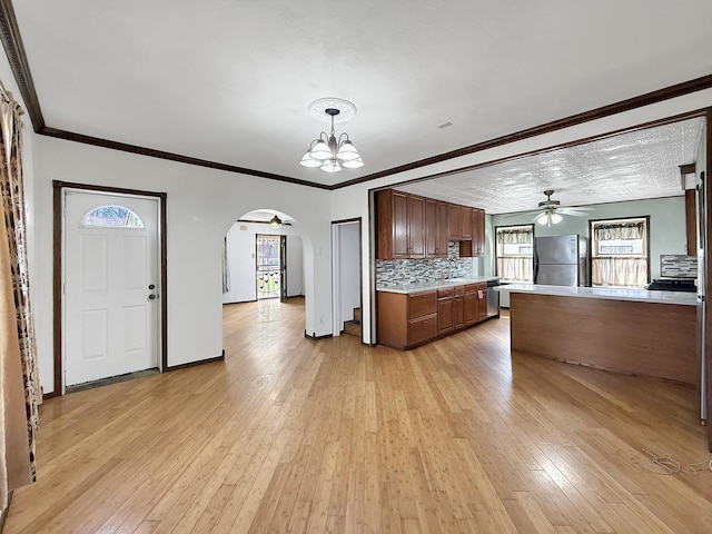 kitchen featuring tasteful backsplash, ceiling fan with notable chandelier, arched walkways, light countertops, and freestanding refrigerator