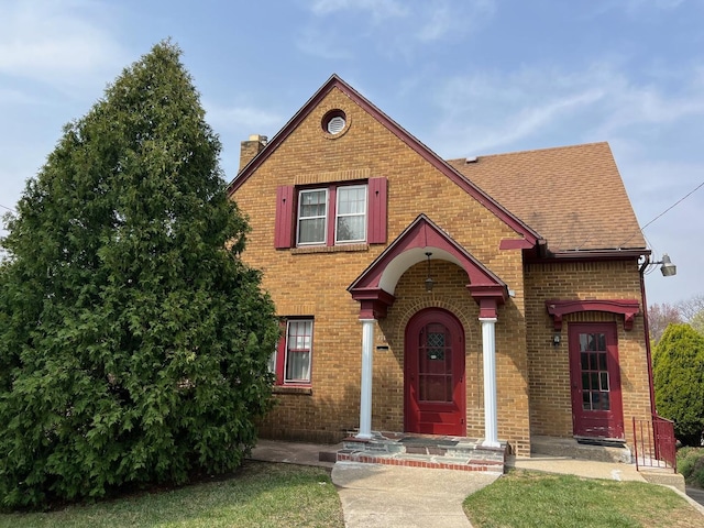 view of front facade with brick siding, roof with shingles, and a chimney