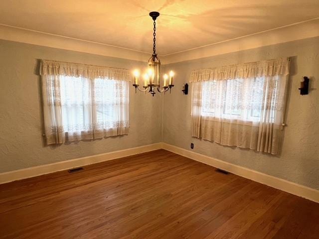 empty room featuring a chandelier, a healthy amount of sunlight, dark wood-type flooring, and visible vents