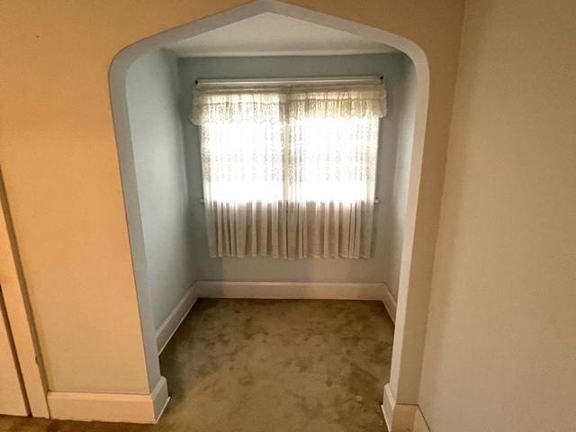 carpeted empty room featuring arched walkways and baseboards
