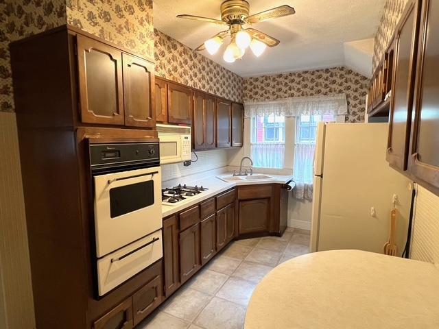 kitchen featuring a sink, a warming drawer, wallpapered walls, white appliances, and ceiling fan
