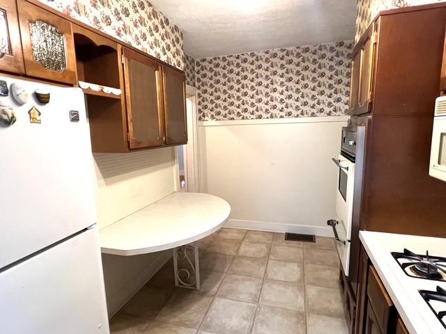 kitchen featuring wallpapered walls, light countertops, open shelves, white appliances, and wainscoting