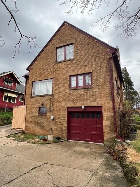 view of side of property featuring brick siding, an attached garage, and concrete driveway