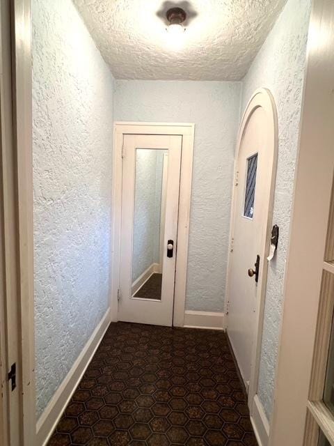 doorway to outside featuring a textured wall, a textured ceiling, and baseboards