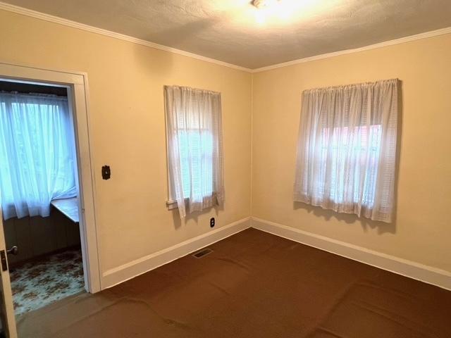 unfurnished room with dark carpet, a healthy amount of sunlight, baseboards, and ornamental molding
